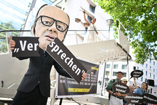 Ein Aktivist mit Merz-Maske zerbricht während einer symbolischen Protestaktion von Kabul Luftbrücke und Campact zur Unterstützung von Klagen von Afghanen gegen die Bundesregierung vor dem Auswärtigen Amt ein Schild mit der Aufschrift „Versprechen“. Im Hin