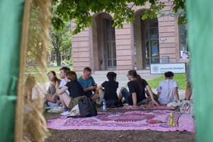 Studierende sitzen auf Decken auf dem Boden vor einem Gebäude der Uni Stuttgart.