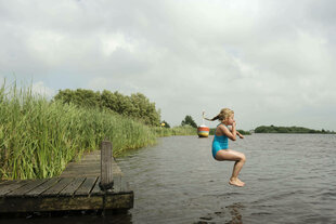 Ein Mädchen springt von einem Steg in einen See