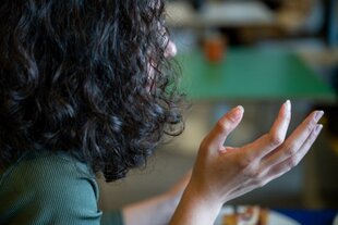 Über die Schulter ist eine Person zu sehen mit angehobener Hand, das dunkle lange Haar verbirgt ihr Gesicht.