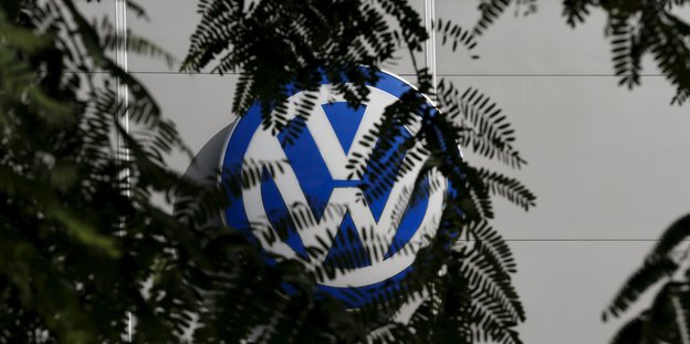 Ein VW-Logo wird zum Teil von Blättern verdeckt.