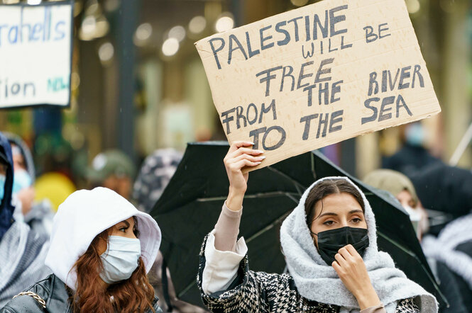 Eine Demonstrantin hält ein Schild in die Luft, auf dem der Spruch in abgeänderter Reihenfolge steht.