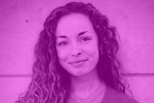 Porträt von Katja Schubel mit lockigem Haar vor einer Wand, schmunzelnd, mit direktem Blick in die Kamera. Das Foto ist eingefärbt in das markante Magenta des Dissens-Podcasts.