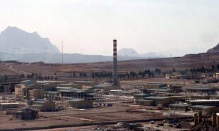 Mehrere Gebäude und ein großer Schornstein in einer Wüstenlandschaft, im Hintergrund ein Gebirgszug