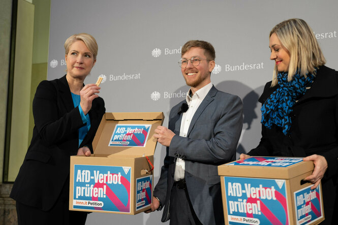 Drei Personen auf einer Bühne halten Kartons mit der Aufschrift "AfD-Verbot prüfen"