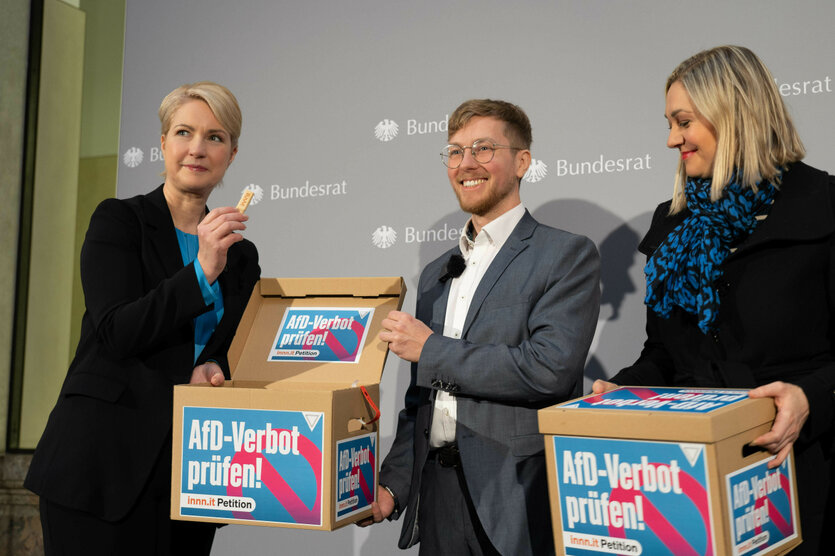 Drei Personen auf einer Bühne halten Kartons mit der Aufschrift "AfD-Verbot prüfen"