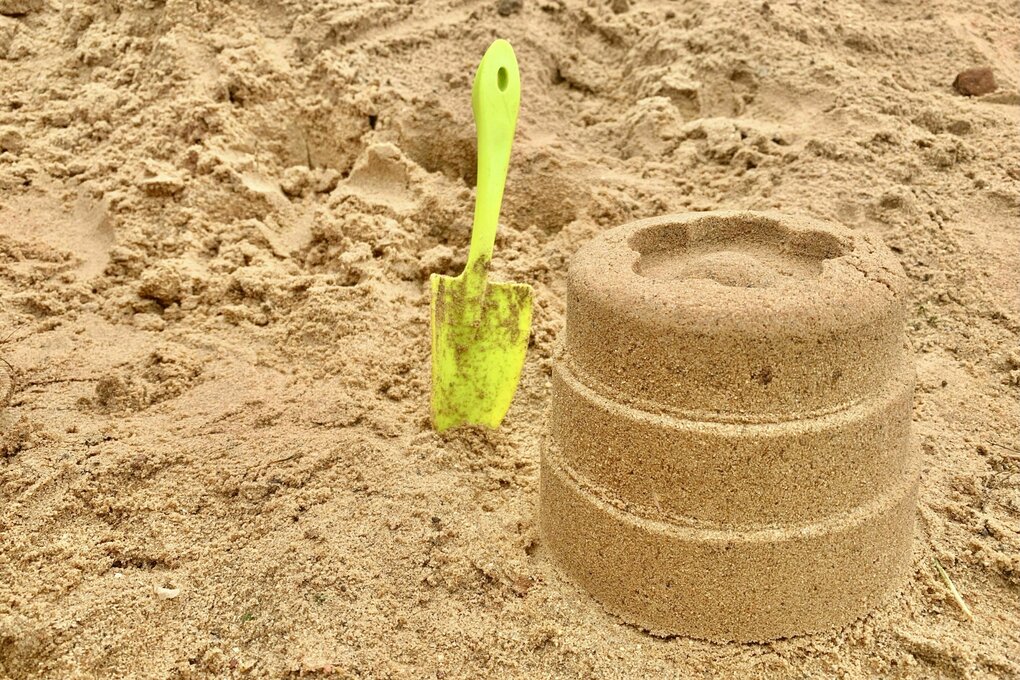 Ein Sandkuchen neben einer Schaufel am Strand
