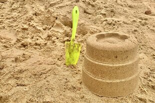 Ein Sandkuchen neben einer Schaufel am Strand