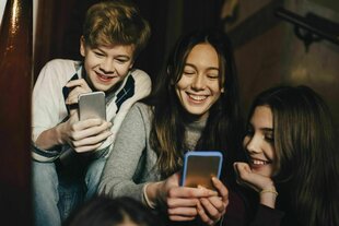 Jugendliche sitzen auf einer Treppe und schauen in ihre Handy