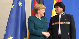 Merkel und Morales schütteln sich die Hand. Im Hintergrund Fahnen.