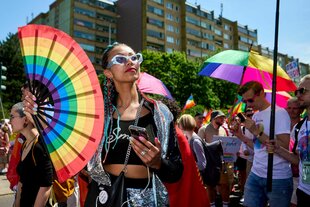 Eine Person mit einem großen Handfächer mit Regenbogenmotiv