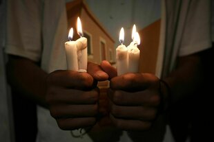 Eine Person hält vier brennende Kerzen in den Händen: Syrische Christen protestieren mit Kerzen vor einer Kirche in Zentralsyrien gegen den Selbstmordanschlag in Damaskus
