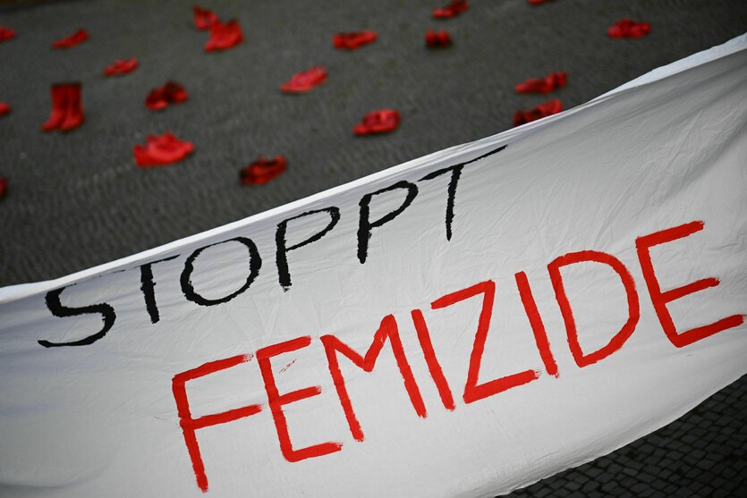 "Stoppt Femizide" steht auf einem Banner vor roten Schuhen, dem Symbol des Kampfes gegen Gewalt an Frauen