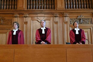 Drei RichterInnen in roten Roben stehen vor einer holzvertäfelten Wand