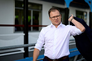 Carsten Schneider in sommerlichem Hemd, ohne Krawatte, das Sacko über die Schulter werfend