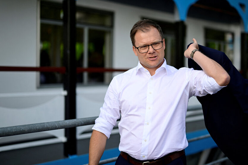Carsten Schneider in sommerlichem Hemd, ohne Krawatte, das Sacko über die Schulter werfend