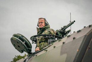 Boris Pistorius in Uniform und mit Kopfhörern schaut aus einem Panzer