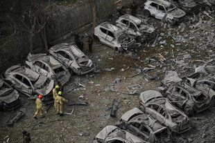 Luftbild von zwei Feuerwehrkräften, die auf einem Platz zwischen zwei Reihen von verkohlten Autos laufen
