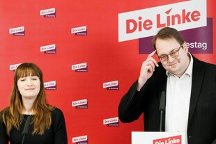 Heidi Reichinnek und Sören Pellmann stehen nebeneinander vor einer Wand mit dem Logo der Linken