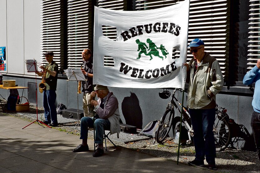 Zwei Personen stehen vor einem Gebäude und halten ein Transparent mit der Aufschrift "Refugees Welcome".