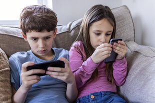 2 Kinder auf Sofa, auf Smartphones blickend