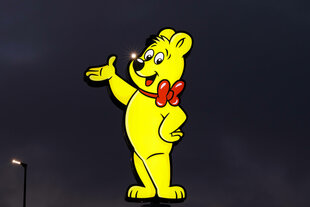 Ein gelbes Haribo-Gummibärchen leuchtet als Reklamefigur in der Dunkelheit
