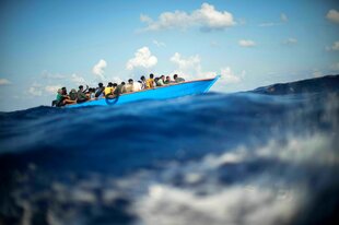 Migranten sitzen in einem Holzboot im Mittelmeer.