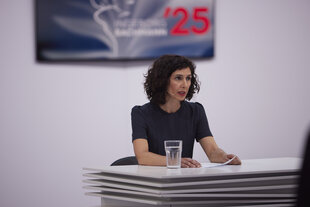 Eine Frau in dunklem Oberteil sitzt an einem weißen Tisch