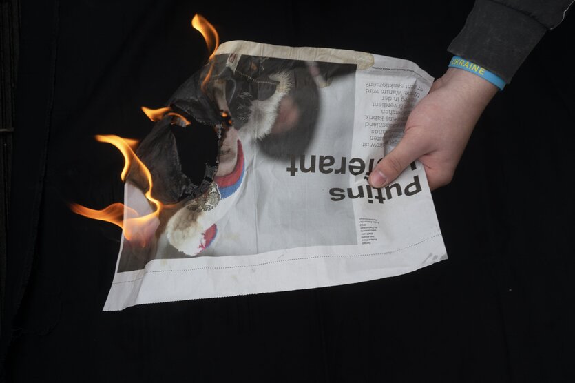 Eine brennende Zeitung wird vor einem schwarzem Hintergrund mit einer Hand gehalten.