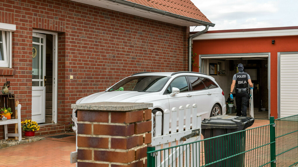 Ein Wohnhaus, ein Auto und eine uniformierte Person.