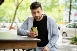 Wael Aljasim, Geflüchteter aus Syrien sitzt am Tisch eines Straßencafes und schaut auf sein Smartphone