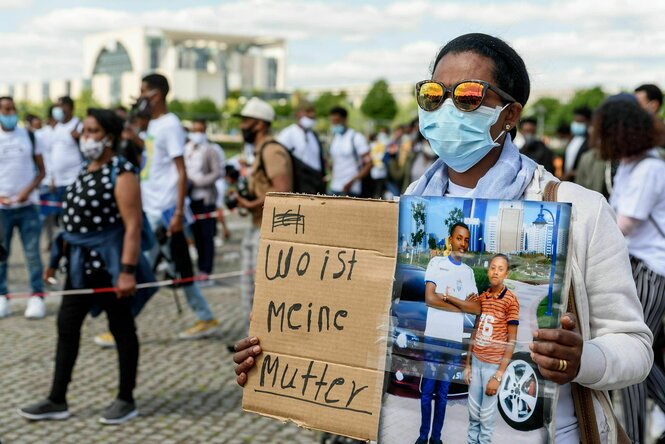 Protestaktion vor dem Bundeskanzleramt in Berlin: Eine Frau, die eine Gesichtsmaske träft zeigt auf einem Plakat fotos von zwei Jungen, links steht "Wo ist meine Mutter"