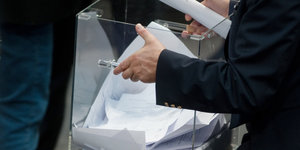 Ein Mann trägt eine gläserne Urne mit Stimmzetteln.