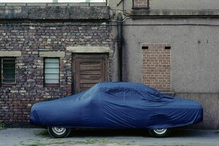 Abgestelltes Auto, das mit einem blauen Überzug versehen ist, steht in einem tristen Hinterhof