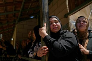 Eine trauernde Frau umrahmt einen Holzpfosten an einem Haus