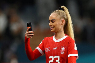 Eine Spielerin im Schweizer Trikot steht mit Handy auf dem Platz