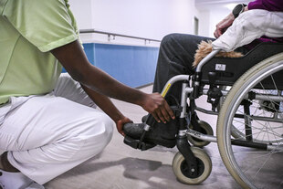 Ein Pflegehelfer montiert die Fußstützen am Rollstuhl einer Frau Ein Pflegehelfer montiert die Fußstützen am Rollstuhl einer Frau