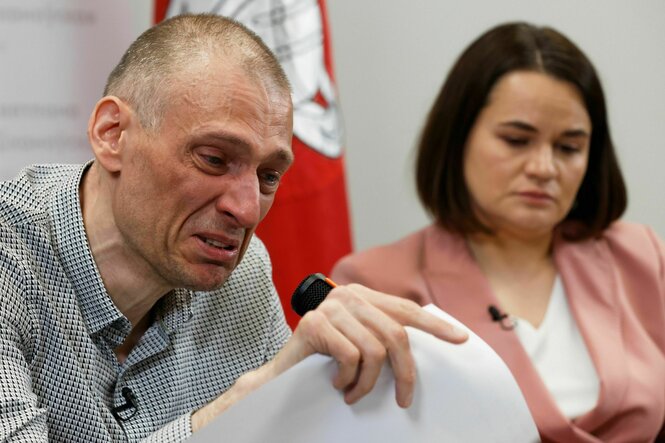 Ein Mann und eine Frau sitzen nebeneinander. Der Mann spricht unter Tränen mit Vertretern der Presse