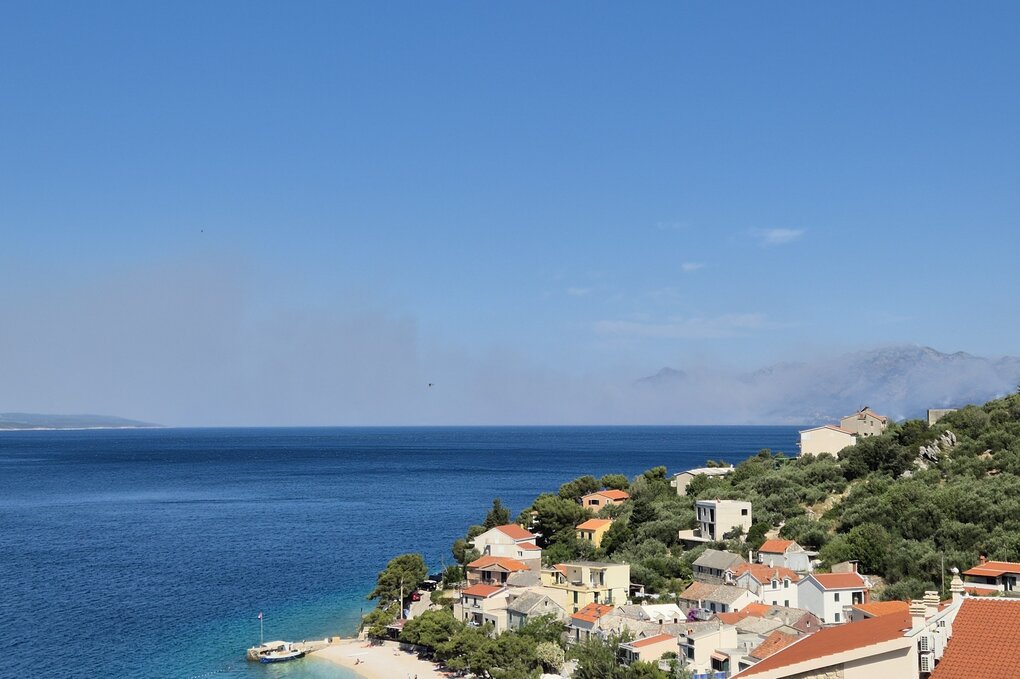 Am Horizont sind Rauchwolken zu sehen, die von einem großen Waldbrand verursacht werden.