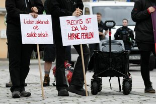 Teilnehmer einer Kundgebung der Partei Die Linke stehen auf dem Marktplatz und halten Schilder mit der Aufschrift "Lieber solidarisch als solide arisch" und "Rechts ist da wo Hirne fehlen"