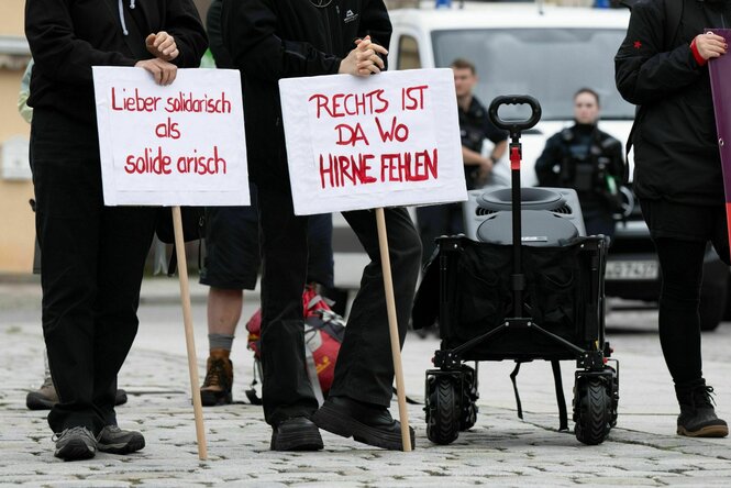 Teilnehmer einer Kundgebung der Partei Die Linke stehen auf dem Marktplatz und halten Schilder mit der Aufschrift "Lieber solidarisch als solide arisch" und "Rechts ist da wo Hirne fehlen"