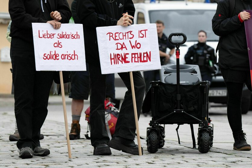Teilnehmer einer Kundgebung der Partei Die Linke stehen auf dem Marktplatz und halten Schilder mit der Aufschrift "Lieber solidarisch als solide arisch" und "Rechts ist da wo Hirne fehlen"