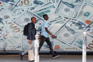 Vor einer Wechselstube in der Innenstadt von Nairobi laufen Menschen an einem Bild von US-Dollar-Scheinen vorbei