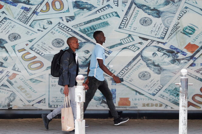 Vor einer Wechselstube in der Innenstadt von Nairobi laufen Menschen an einem Bild von US-Dollar-Scheinen vorbei