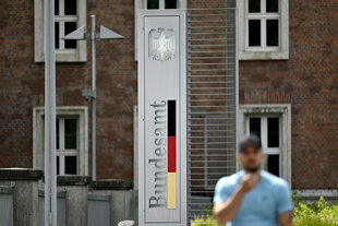 Ein Mann steht vor einem Haus, an einer Säule steht "Bundesamt"