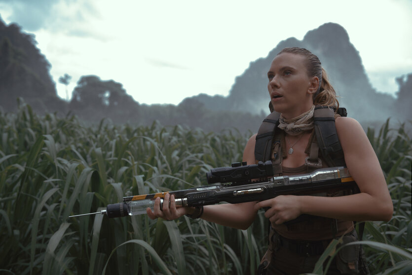 Die Schauspielerin Scarlett Johannson mit einem Gewehr im Arm, an deren Spitze eine Spritze steckt
