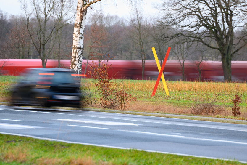 Ein Auto und ein Zug fahren an einem gelb-roten "x" auf einer Wiese vorbei