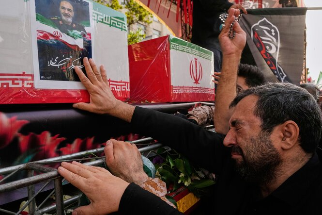 Ein weinender Mann berührt mit seiner rechten Hand den Sarg eines iranischen Miltärführers, der auf einem Lastwagen aufgebahrt ist. Der Sarg ist mit einer iranischen Fahne bedeckt