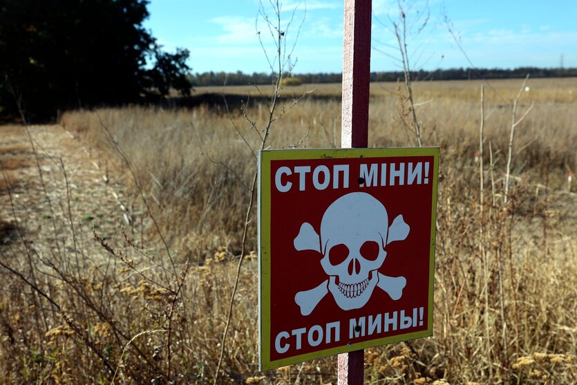 Ein Schild an einem Pfosten vor einem Feld, das auf Ukrainisch vor Minen warnt