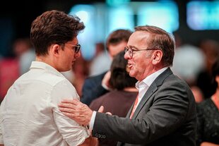 Zwei Männer stehen sich gegenüber und legen sich die Arme auf die Schultern